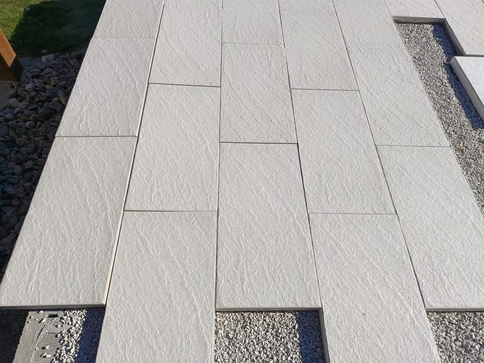 Detail světlé velkoformátové venkovní dlažby se štěrkovým lemem